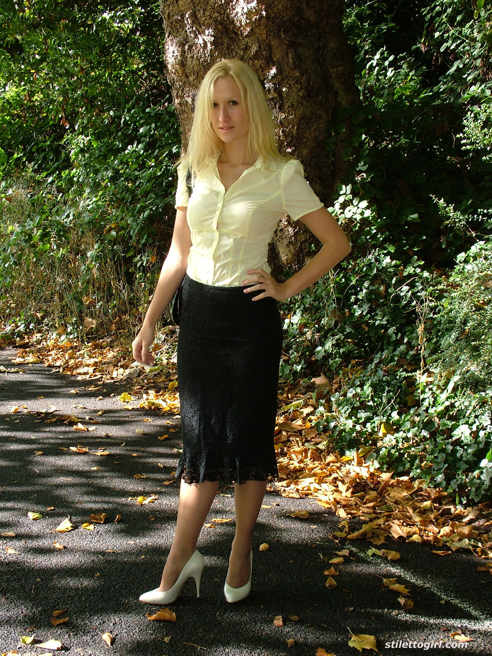 clothed blonde iona shows off her white stilettos in a long skirt by a park