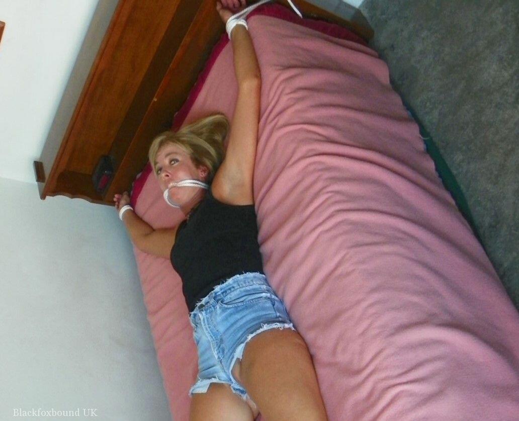 clothed female is gagged while tied up with rope on a single bed
