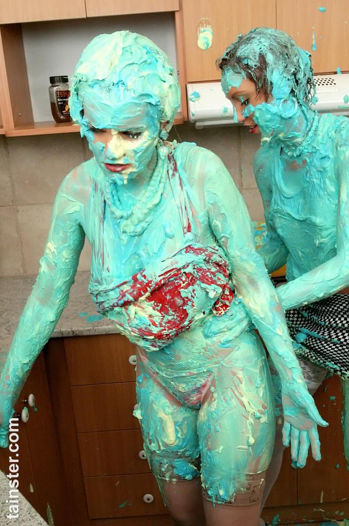 clothed women cover each other in cake mix during a food fight in kitchen