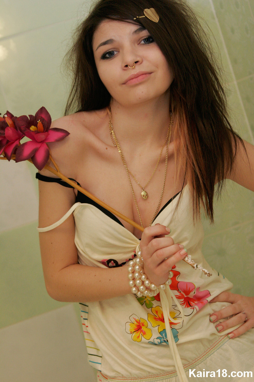 cute girl kaira 18 holds a stalk of flowers while posing clothed in a bathroom
